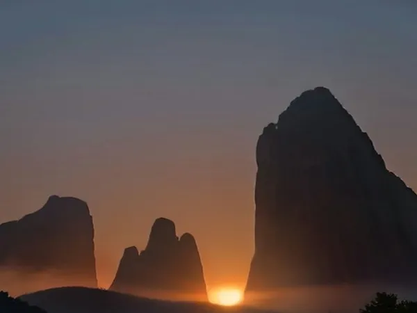 Rock pillars glowing orange at sunset with a monastery silhouette