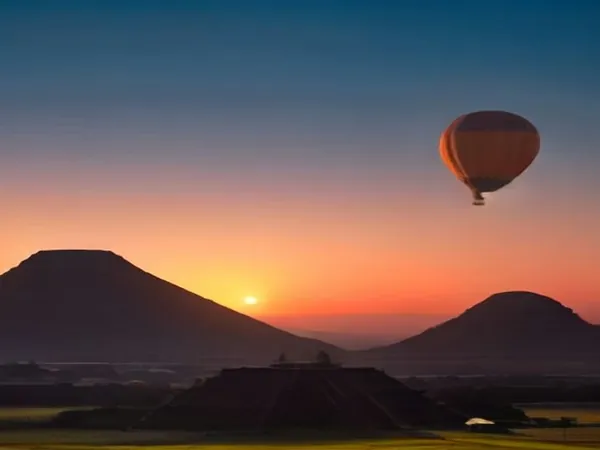 A hot air balloon in an orange sunrise sky above pyramid-shaped hills