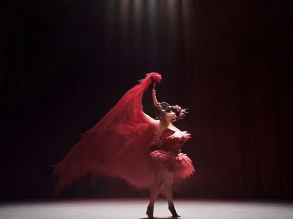 A cabaret dancer in a red feathered costume under a spotlight on a dark stage
