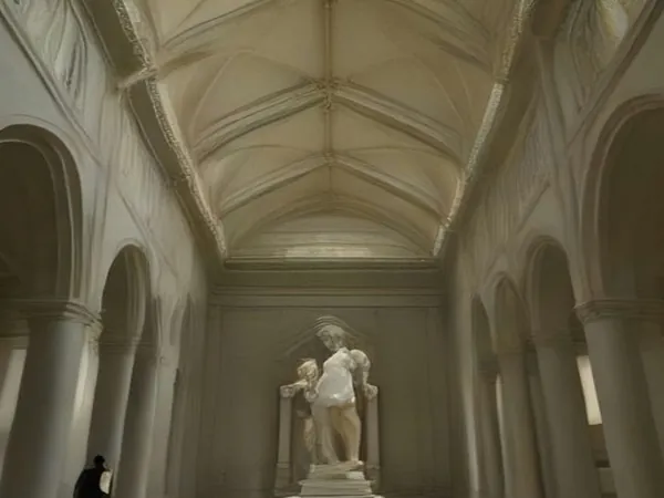 A grand vaulted museum gallery with a classical marble statue and a lone visitor